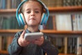 Cute Caucasian little girl in big white headphones listens music in the interior against the background of bookshelves Royalty Free Stock Photo