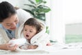 Cute Caucasian little toddler baby girl wear bathrobe after bathing is smiling and lying while mother apply  talcum powder on her Royalty Free Stock Photo