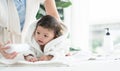 Cute Caucasian little toddler baby girl wear bathrobe after bathing is smiling and lying on towel. mom apply talcum powder on body Royalty Free Stock Photo