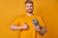 Cute caucasian positive young guy holding a gym mat and showing thumbs up