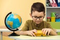 Cute caucasian schoolboy wearing glasses and sits at a desk in the classroom at elementary school. Little boy next the Globe Royalty Free Stock Photo