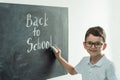 Cute caucasian schoolboy wearing glasses and writing Back to school text on the black school board Royalty Free Stock Photo