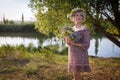 Cute caucasian woman stands on the bank of the river with a bouquet of wild flowers at sunset