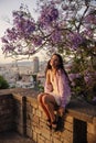 Cute caucasian young girl smiling looking at camera, sitting on fence near flowering tree in spring. Royalty Free Stock Photo