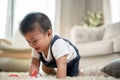 A cute, cheerful Asian baby boy is playing with toys and crawling on the floor in the living room Royalty Free Stock Photo