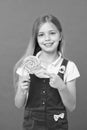 Cute cheerful girl holding giant candy. Kid with long blond hair isolated on violet background. Child pointing at