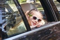 Cute cheerful little caucasian girl sitting inside the car, looking out the window and smiling at the camera. Family Royalty Free Stock Photo