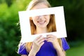 Cute cheerful little girl holding white picture frame in front of her face