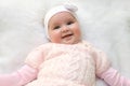 Cute cheerful newborn dressed in pink sweater on white fur blanket. Adorable infant baby with headband. Royalty Free Stock Photo