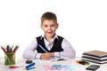 Cute cheerful pupil sitting still at the desk, surrounded with stationery