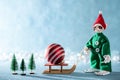 Cute Cheerful Santas Helper Elf Pulling Santas Sleigh With Christmas Bauble.North Pole Christmas Scene. Elf at work.