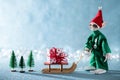 Cute Cheerful Santas Helper Elf Pulling Santas Sleigh With Christmas Present. North Pole Christmas Scene. Santas Workshop.