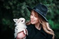 Cute cheerful slim caucasian girl blonde with long hair in a black coat and a black hat in in the autumn day with her white small