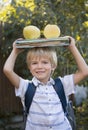cute cheerful 6 year old boy holding stack of books and two big apples on his head, getting ready to go to school Royalty Free Stock Photo