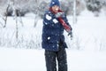 Cute, cheerful young boy in hat, blue jacket plays with snow, has fun, smiles, makes snowman in winter park. Royalty Free Stock Photo