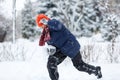 Cute, cheerful young boy in hat, blue jacket plays with snow, has fun, smiles, makes snowman in winter park. Royalty Free Stock Photo