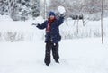 Cute, cheerful young boy in hat, blue jacket plays with snow, has fun, smiles, makes snowman in winter park. Royalty Free Stock Photo