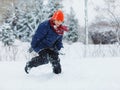 Cute, cheerful young boy in hat, blue jacket plays with snow, has fun, smiles, makes snowman in winter park. Royalty Free Stock Photo