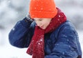 Cute, cheerful young boy in hat, blue jacket plays with snow, has fun, smiles, makes snowman in winter park. Royalty Free Stock Photo