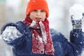 Cute, cheerful young boy in hat, blue jacket plays with snow, has fun, smiles, makes snowman in winter park. Royalty Free Stock Photo