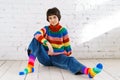 Cute cheerful young girl in colorful sweater, sitting on floor against Royalty Free Stock Photo