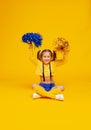 Cute cheerleader girl in a yellow tank and blue shorts holds pompons