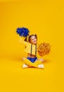 Cute cheerleader girl in a yellow tank and blue shorts holds pompons