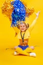 Cute cheerleader girl in a yellow tank and blue shorts throws up pompons
