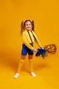 Cute cheerleader girl in a yellow tank top and blue shorts is dancing with pompons in her hands