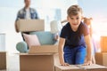 Cute child with box with his family packing belongings at home. Moving into new house