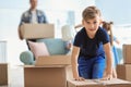 Cute child with box with his family packing belongings at home. Moving into new house