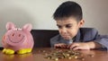 Cute child, boy in a business suit with sad face expression looking at piggy bank and coins. Recesion, negative