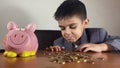 Cute child, boy in a business suit with sad face expression looking at piggy bank and coins. Recesion, negative