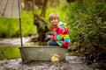 Cute child, boy in colorful jacket, playing with boat and ducks on a little river, sailing and boating. Kid having fun, childhood