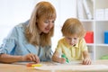 Cute child boy drawing and writing with colorful markers pens at kindergarten. Creative kid painting at playschool. Teacher helps