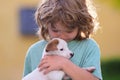 Cute child boy feels delighted, closes eyes from pleasure, carries little baby dog, expresses tender emotions, care and Royalty Free Stock Photo
