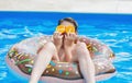 Cute child boy on funny inflatable donut float ring in swimming pool with oranges. Teenager learning to swim Royalty Free Stock Photo