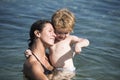 Cute child boy play with water in ocean, sea. Motherhood concept. Mother carries son in hands, hugs child. Mom and kid Royalty Free Stock Photo