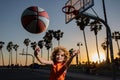 Cute child boy plays basketball. Active kids enjoying outdoor game with basketball ball on Venice beach basketball court Royalty Free Stock Photo