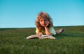 Cute child boy reading book outdoor on green grass field. Smart child reading book, laying on grass summer park on sky Royalty Free Stock Photo