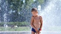 Cute child, a boy of seven years having fun, bathes in a fountain and playing water splash in outside, on a hot summer