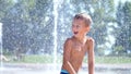 Cute child, a boy of seven years having fun, bathes in a fountain and playing water splash in outside, on a hot summer