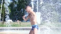 Cute child, a boy of seven years having fun, bathes in a fountain and playing water splash in outside, on a hot summer