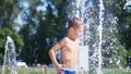 Cute child, a boy of seven years having fun, bathes in a fountain and playing water splash in outside, on a hot summer