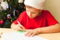 Cute child boy write letter to Santa, Christmas tree on background