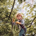 Cute child in climbing safety equipment in a tree house or in a rope park climbs the rope. Happy little child climbing Royalty Free Stock Photo