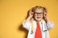 Cute child in doctor coat with stethoscope on color background.