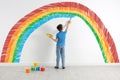 Cute child drawing rainbow on white wall