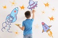 Cute child drawing spaceships on white wall