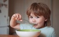 Cute child eating breakfast at home. Parenthood. Baby eating. Young kid sitting on the table eating with funny Royalty Free Stock Photo